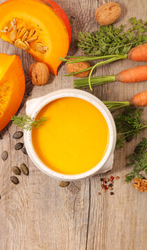 Pumpkin and Carrot Soup with Fresh Ingredients, Squash Slices, and Walnuts on Wooden Background