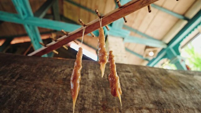 Freshly dipped churchkhela hang from a wooden rod to dry under the painted timber roof of a Georgian winery kitchen.