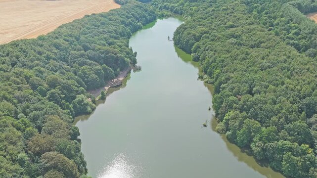 Newmillerdam lake extends between dense woodland and cultivated farmland at Newmillerdam Country Park, Wakefield, West Yorkshire, England, Europe, drone forward flyover