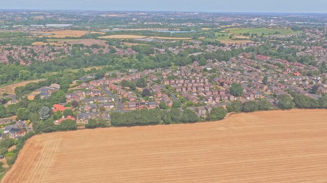 Newmillerdam Country Park harvested cereal field borders residential development near Wakefield, West Yorkshire, England, with parallel combine lines visible, drone lateral slide.