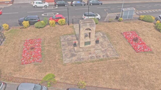 Greasbrough War Memorial stands amid red poppy beds on Church Street, Greasbrough, Rotherham, South Yorkshire, England, commemorating local losses in two world wars, drone descent push in