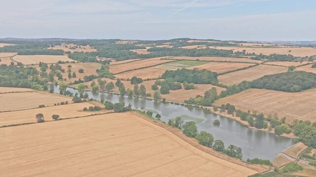 River Don winds through harvested arable fields and wooded riparian corridors near Greasbrough, Rotherham, South Yorkshire, England, forming a rural floodplain landscape, drone forward flyover
