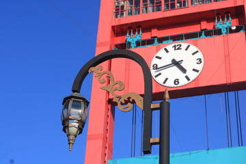 A tall red gateway on Ampera Bridge with a prominent round clock in the middle, showcasing a striking and symmetrical design © Opran