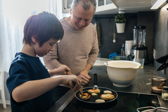 Father and son cooking pancakes together in kitchen