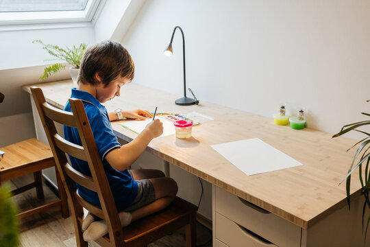 Young boy painting watercolor at home desk