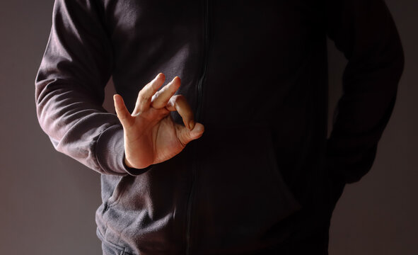 Cropped shot of an Asian man wearing a black sweater, gesturing an OK sign, symbolizing success and approval in a dark setting. Concept of positive non-verbal communication, close-up.