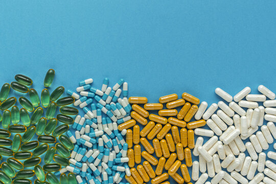 Assorted vitamin capsules and softgels line blue background with copy space for healthcare, nutrition and supplement concepts.