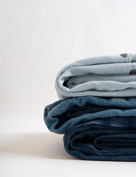 A stack of neatly folded denim jeans in various shades of blue against a clean light background with copy space.