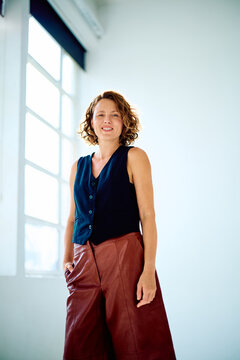 Woman with curly hair posing in a waistcoat and brown leather culottes, expressing confidence and modern fashion
