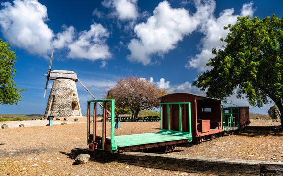 Historic stone windmill and old sugar cane transport train cart at Betty's Hope plantation under a blue sky in Antigua and Barbuda.