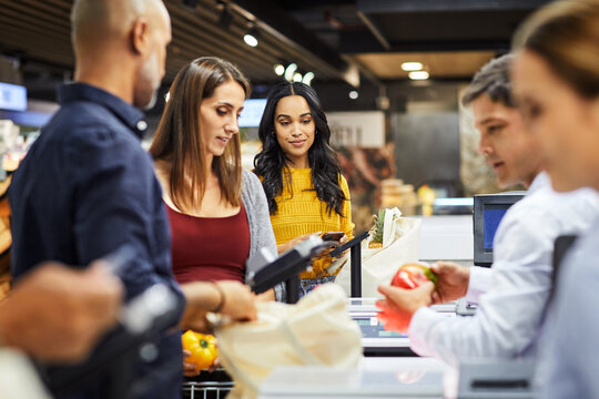 Pos machine, grocery and queue with woman in supermarket for shopping, retail and sales. Digital transaction, discount and food coupon with people in store for customer, line and promotion code