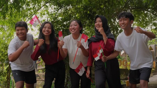 Five joyful young Indonesian people is holding country flags while hugging each other. Indonesian Independence Day concept.