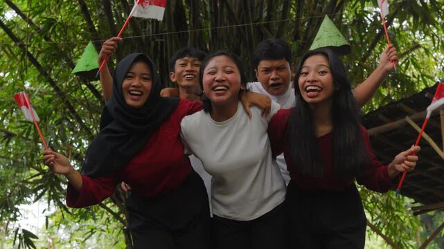 Five joyful young Indonesian people is holding country flags while hugging each other. Indonesian Independence Day concept.