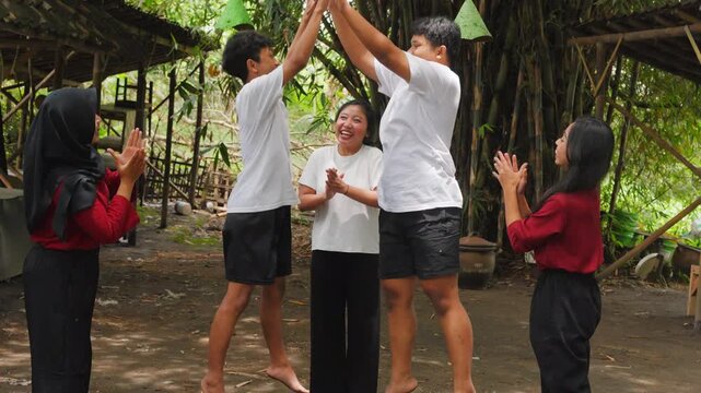 Group of excited young Indonesian teenagers doing high five and raising arms in celebration. Indonesian Independence Day concept.