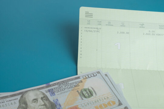 Close up of a bank savings passbook and US dollar bills on a blue background with copy space. Concept of personal finance, saving money, wealth management, banking and financial planning.