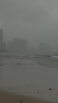 A foggy beach scene with dark waves and distant skyscrapers. The atmosphere is gloomy and overcast, creating a sense of calm and solitude.
