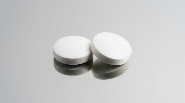 Pharmaceutical drug discovery concept with two white tablets on reflective surface evokes clinical research and medical innovation