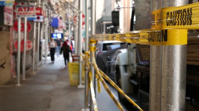 Caution yellow tape and scaffolding on pavement under construction in Manhattan, New York City, United States. Renovation or maintenance, strip barricade or barrier ribbon, scaffold safety warning.