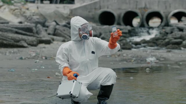 Scientist in full gear kneels by polluted water. He holds a sample vial, eyes focused. Background shows broken pipes and debris