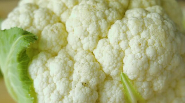 Macro close up of white cauliflower head with green leaves, carefully arranged for vibrant culinary presentation highlighting natural textures, vivid seasonal produce, wholesome n