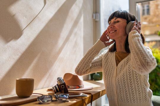 A cheerful girl listens to music on headphones. A girl with a short haircut, wearing headphones, enjoys her favorite song and smiles in a cafe.