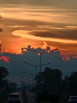 A dramatic twilight sky painted in brilliant shades of orange and gold as the sun sets behind dark, silhouetted clouds.