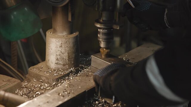 Rotating drill bit cuts metal block in vise in dim workshop, warm light, scattered shavings, tight closeup machinery detail precision metalworking process
