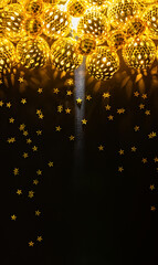 Fototapeta premium Vertical golden Christmas ball lights and scattered stars on black background with copy space for New Year greeting or festive poster