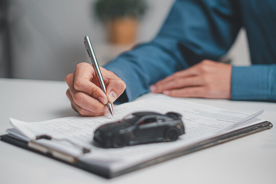 Close up of customer hand signing car loan application and auto insurance contract with toy car.