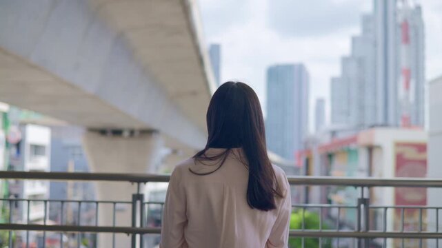 sad lonely teen girl standing on a bridge looking at blurred urban skyscrapers city buildings as a conceptual backdrop for youth mental health solitude city exploration lifestyle and modern commuter 
