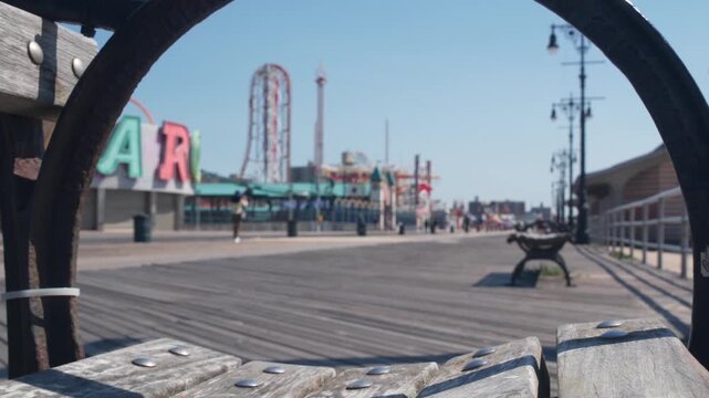 Coney Island beach promenade in Brooklyn, New York, United States. Wooden boardwalk near retro luna park. Amusement park on ocean coast beach. Waterfront summer holiday, people walking on promenade.