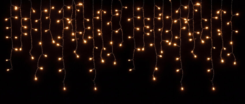 Fairy lights hanging garland with warm glow featuring luminous orange and golden bulbs on vertical wires over a dark backdrop for festive Christmas banners and seasonal celebration decor