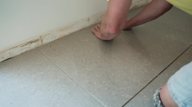 Worker presses a freshly installed floor tile firmly into place by hand, seating it into the adhesive and aligning the surface during interior renovation.