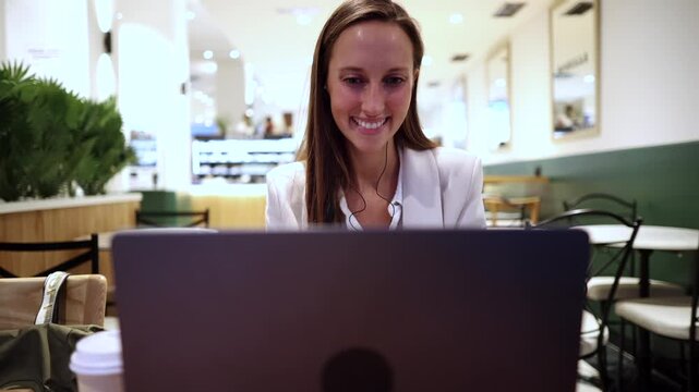 Young woman smiling while concentrating on her work using a laptop computer, enjoying a casual business environment at a stylish coffee shop, representing remote work and productivity