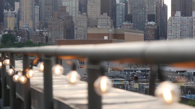 New York City Manhattan Midtown skyline from Queens, United States. Skyscraper buildings architecture, cityscape from rooftop in Long Island, Hunters Point. Light bulbs garland on roof, urban sunset.