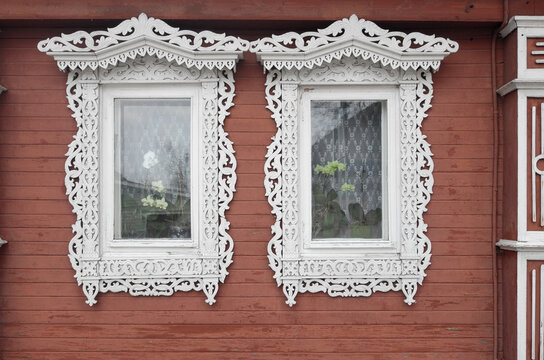 Ornate Carved White Window Frames on Red Wooden Russian House With Lace Curtains