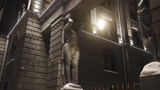 Ornate historic stone facade at night with carved statues, glowing wall lamp, deep shadow, snow tipped ledges, low angle urban passage, elegant architecture, moody heritage atmosphere
