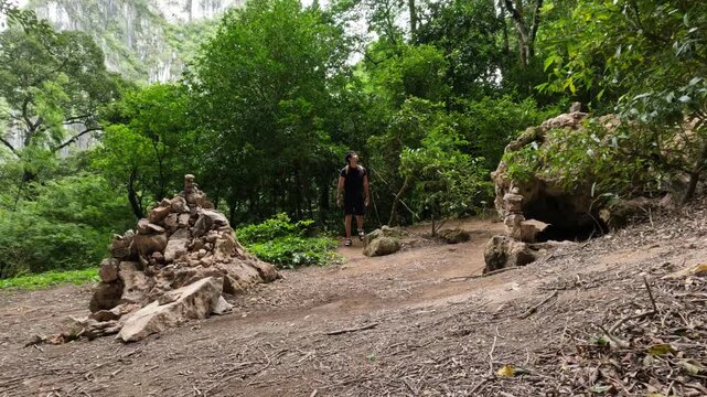 Asian man exploring a forest trail with stacked stones in tropical Thai nature.