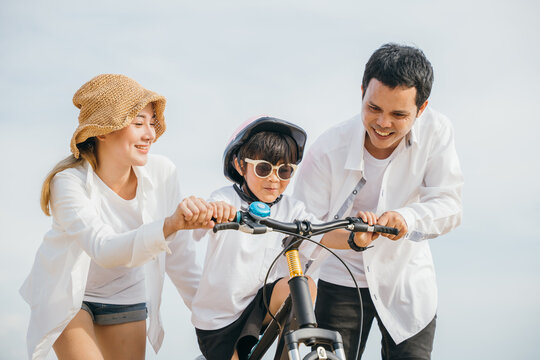 As sun sets cheerful family embraces joy of summer on sandy beach. Parents teach their children to ride bicycles capturing carefree happiness of safety freedom and family love.