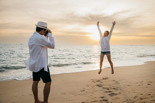 Love in focus as young couple dressed in white enjoys sunrise date on beach. boyfriend armed with camera lovingly captures snapshots of his girlfriend creating memories by ocean.