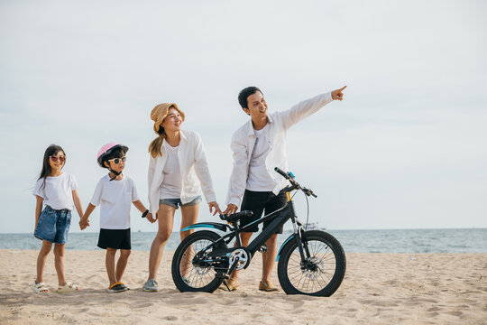 Parents and children walking on the beach pushing bicycles a full-length family scene of happiness joy and the carefree spirit of childhood enjoying the sun and sea. Family on beach vacation