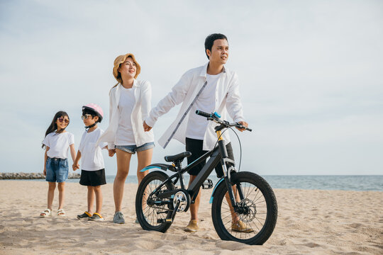 Parents walking on the sandy beach pushing their bicycles a scene full of family joy smiles and the inspiration of a carefree childhood. Family on beach vacation