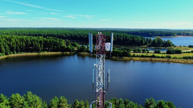 Cellular tower standing on a lakeside with lush green forest backdrop and serene blue water