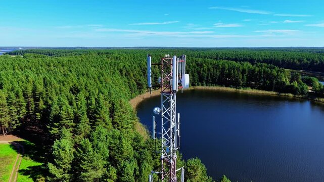Aerial view of cellular tower beside lake with dense forest and clear blue sky