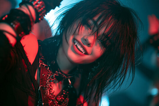 Modern Vampire Woman with Fangs and Black Punk Outfit Smiling During an Energetic Neon Halloween Party