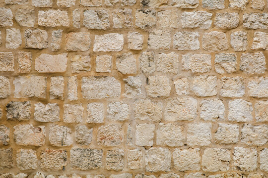 Light beige natural stone wall texture. Ancient rough limestone blocks background. Background of an old fortress wall made of uneven light beige limestone blocks. Rough stone masonry texture