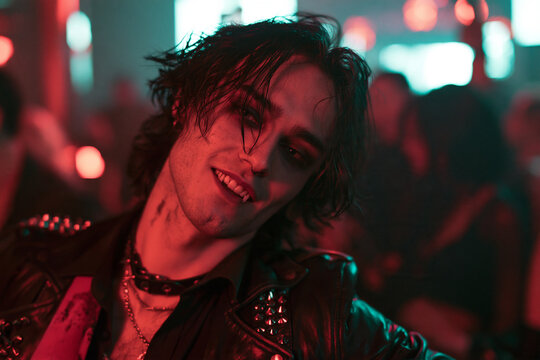 Modern Vampire Man Wearing Punk Leather Jacket and Fangs at Neon Halloween Nightclub Party with Gothic Style