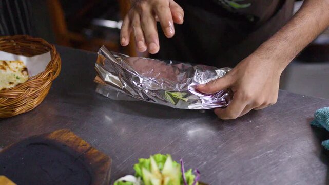 Chef Wrapping Fresh Indian Naan Bread in Aluminum Foil for Takeaway