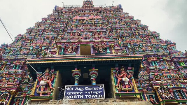 4K video panning upward from the base to the top of the ornate gopuram of Meenakshi Amman Temple in Madurai, Tamil Nadu, India, revealing intricate sculptures and colorful Dravidian architecture.