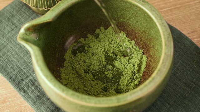 Pouring hot water into ceramic bowl with bright green matcha powder. Healthy detox superfood beverage preparation of Japanese green tea or matcha latte.